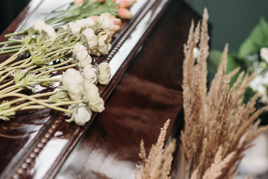 A close-up of a floral arrangement placed on a polished dark wood surface, showcasing white lisianthus flowers with delicate, soft petals and slender green stems. The flowers are arranged in a linear 